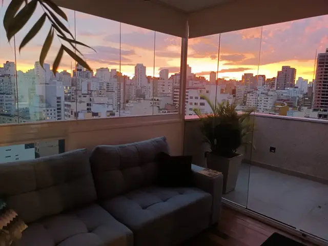 Varanda envidraçada de apartamento em Higienópolis ao pôr do sol, com vista para os prédios