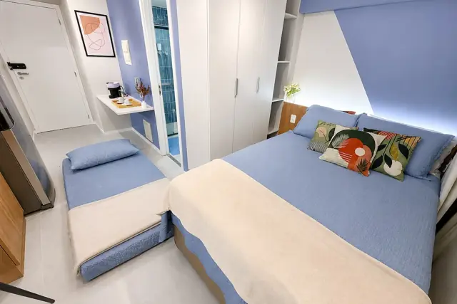Studio do Hub em Santo Amaro: cama de casal com roupa azul e creme, sofá-cama e parede azul